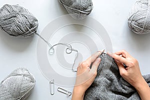 Girl knits gray sweater knitting needles on gray wooden background. Process of knitting.