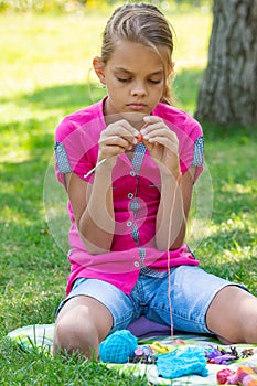 Girl knits on a knitting needles on a picnic in nature