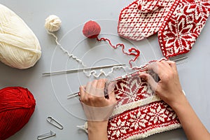 Girl knits red and white jacquard hat knitting needles on gray wooden background. Process of knitting.