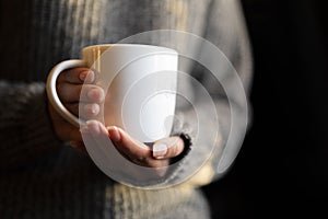 A girl in a knitted sweater holds a white mug