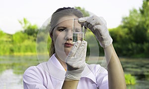 girl laboratory assistant looks at a sample of water in a test tube, recruited from the lake, the concept of ecology