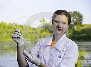 girl laboratory assistant looks at a sample of water in a test tube, recruited from the lake, the concept of ecology