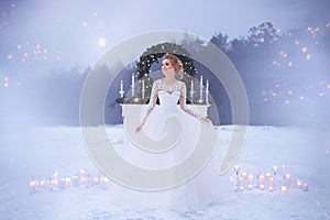 Girl in a lace wedding dress near the fireplace with Christmas decor on the background of snow-covered lake and the night sky.