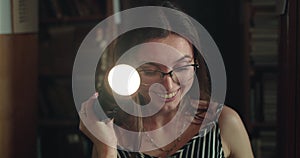 Girl with lantern views library shelves in darkness, is surprised and pulls book