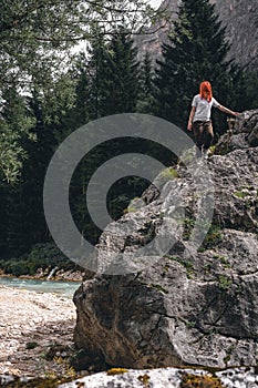 Girl on a large stone, a boulder, among the incredibly beautiful river of turquoise color, pine forest. summer day. vertical photo
