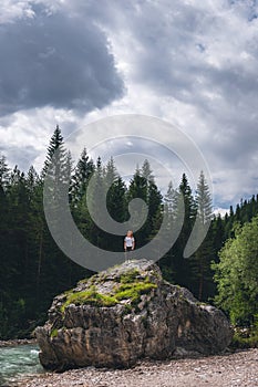 Girl on a large stone, a boulder, among the incredibly beautiful river of turquoise color, pine forest. summer day. vertical photo photo