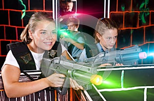 Girl with laser gun having fun on laser tag arena with her teen