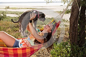 Girl laughing lying in a hammock holding up a small dog, lifestyle