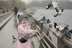A girl laughs and feeds pigeons on the embankment in a city park