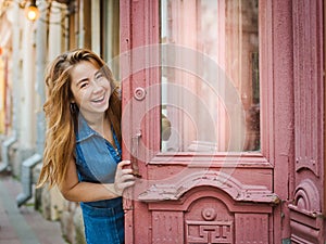 Girl laughs and opens the door to the old house on the street in the city. Free place