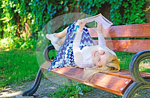 Girl lay bench park relaxing with book, green nature background. Woman spend leisure with book. Girl reading outdoors