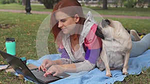 Girl laying and typing on laptop on a lawn with her pug around