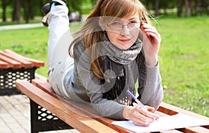 The girl lays on a bench, and writes