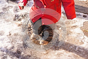 Girl in leahther boots black pants and red jacket standing in a puddle of water splashes snow and ice on warm winter day