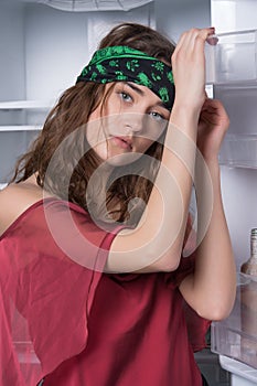 Girl leaning on open fridge door. Skinny model in kitchen, diet concept. Woman with beautiful green eyes and long curly