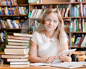 Girl learning in library and reading e-book on tablet computer