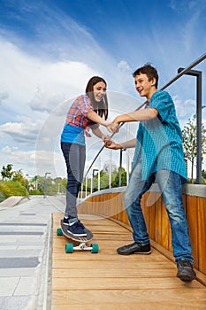 Girl learns riding skateboard holding boy's hands