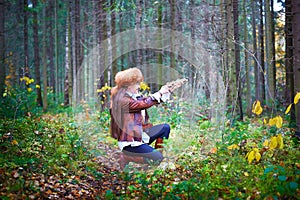 Girl in a leather jacket, a big red fox fur hat and with a crossbow in the forest in autumn. A female model poses as a