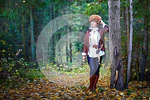 Girl in a leather jacket, a big red fox fur hat and with a crossbow in the forest in autumn. A female model poses as a