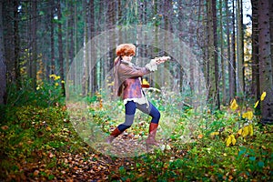 Girl in a leather jacket, a big red fox fur hat and with a crossbow in the forest in autumn. A female model poses as a