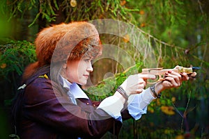 Girl in a leather jacket, a big red fox fur hat and with a crossbow in the forest in autumn. A female model poses as a