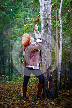 Girl in a leather jacket, a big red fox fur hat and with a crossbow in the forest in autumn. A female model poses as a