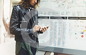 Girl in leather jacket holding smart phone on background map light box in sun atmospheric city, hipster using in female hands