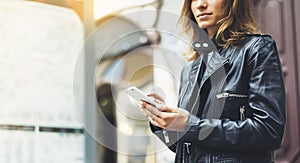 Girl in leather jacket holding smart phone on background map light box in sun atmospheric city, hipster using in female hands