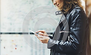 Girl in leather jacket holding smart phone on background map light box in sun atmospheric city, hipster using in female hands