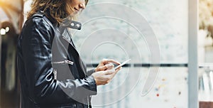 Girl in leather jacket holding smart phone on background map light box in sun atmospheric city, hipster using in female hands