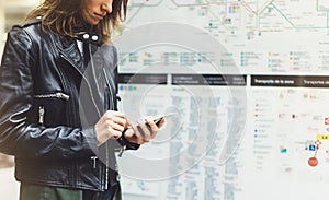 Girl in leather jacket holding smart phone on background map light box in sun atmospheric city, hipster using in female hands