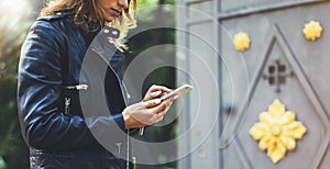 Girl in leather jacket holding smart phone on background sun atmospheric city, hipster using in female hands and texting mobile