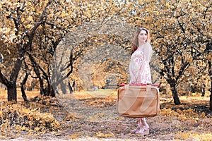 Girl with leather suitcase for travel in the autumn park on walk