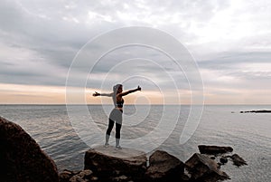 Girl in leggings and a sports top stands on the rocks by the sea at sunset, Gulf of Finland