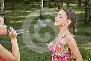 A girl lets out soap bubbles in nature, and a friend catches them.