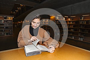 Girl in library turns page of book with smile