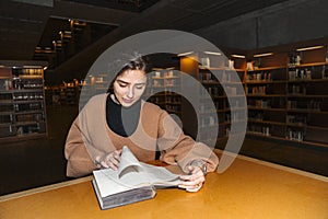 Girl in library turns page of book with smile