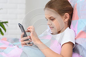 The girl lies in bed and plays in a mobile smartphone