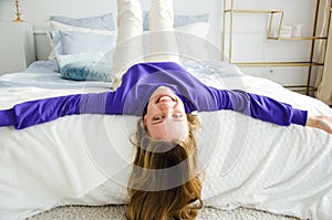 girl lies on the bed upside down in purple sweater and smiles at the camera. concept morning and pampering, childishness photo