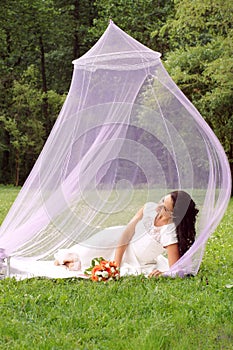 The girl lies in a pink summer airy tent on a lawn