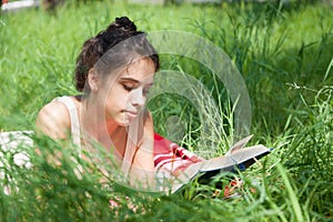 Girl lies on a plaid on the grass and reads a book