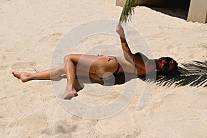 The girl lies on a white sand in a black bikini.