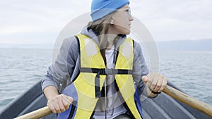Girl in a life jacket, in a blue cap and sunglasses is riding a boat on the lake