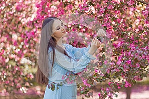 girl in light blue dress is standing near a blooming apple tree