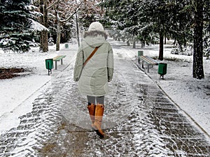 A girl in a light down jacket and orange boots walks along the snowy alley of a winter park. Christmas trees in the snow