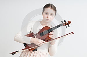 A girl in light dress holding in her hands violin over light background
