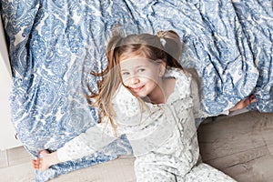 A girl in light gray pajamas lies on a bed by the window, the child woke up