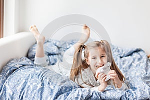 A girl in light gray pajamas sits on a bed by the window, the child woke up in the morning, morning yoga