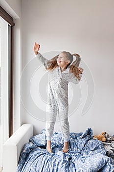 A girl in light gray pajamas stands on the bed, the child woke up