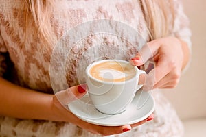 girl in a light knitted sweater sits on a sofa and holds a cup of coffee